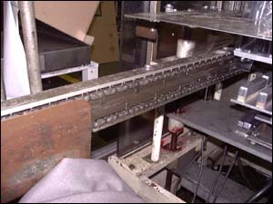 Figure 33. Guard chain rail to prevent access. For illustrative purposes only, the guard has been removed to better see the hazard associated with the pins on the spiked chain and sprocket mechanism used to feed the plastic roll stock through the different stations of the thermoforming machine.